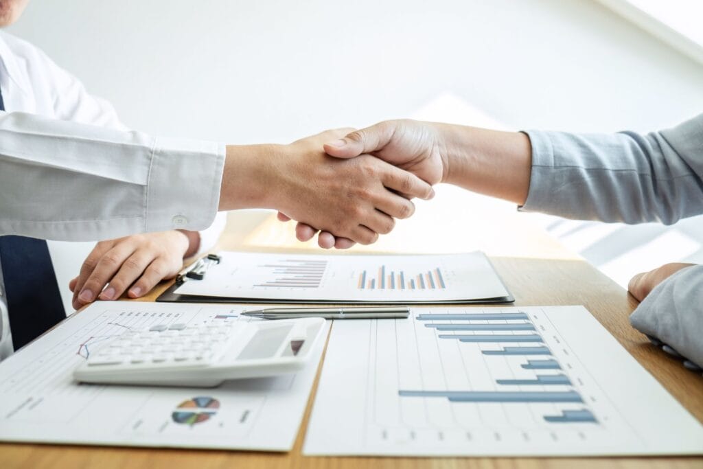 Jabat tangan antara klien dan konsultan pajak SMR di atas meja dengan dokumen keuangan, menunjukkan kesepakatan dan komitmen kerja sama.