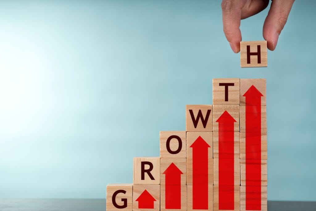 Tumpukan balok kayu bertuliskan "GROWTH" dengan panah merah yang menunjukkan peningkatan, menggambarkan pertumbuhan bisnis.