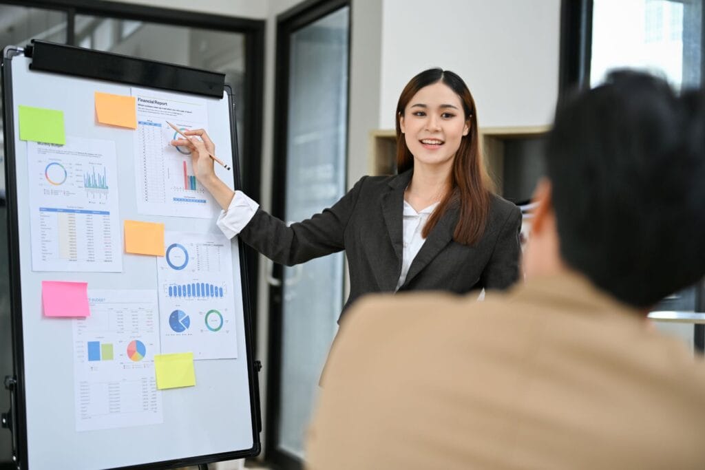 Seorang konsultan pajak SMR sedang mempresentasikan laporan keuangan dan strategi pajak kepada klien di papan tulis dengan grafik dan diagram.